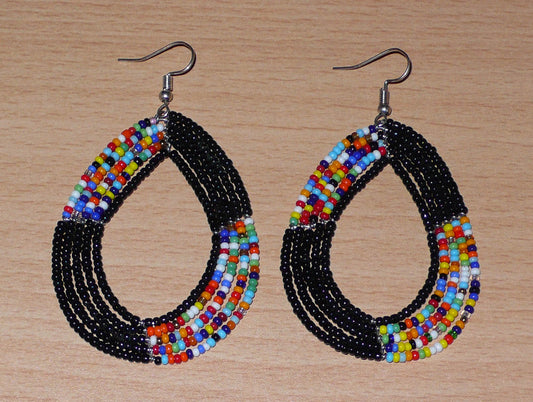 Longues boucles d'oreilles kenyanes évoquant le style bohème hippie chic des années 70 : elles se composent de perles de rocaille noires et multicolores enfilées sur cinq rangées de fils de fer montés en forme de gouttes.  Longues et larges, ces boucles d'oreilles mesurent 8 cm de long sur 5 cm de large ; elles se portent avec des crochets en acier inoxydable sur des oreilles percées.