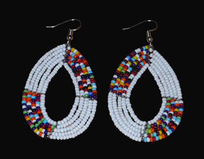 Boucles d'oreilles kenyanes perlées composées de perles de verre blanches et multicolores enfilées sur plusieurs rangées de fils de fer montées en forme de gouttes ovales.  De taille moyenne, ces boucles d'oreilles aux accents exotiques mesurent 7,5 cm de long et 4 cm de large, et se portent avec crochets en acier inoxydable sur des oreilles percées.