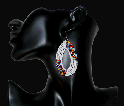 Boucles d'oreilles kenyanes perlées composées de perles de verre blanches et multicolores enfilées sur plusieurs rangées de fils de fer montées en forme de gouttes ovales.  De taille moyenne, ces boucles d'oreilles aux accents exotiques mesurent 7,5 cm de long et 4 cm de large, et se portent avec crochets en acier inoxydable sur des oreilles percées.