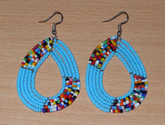 Boucles d'oreilles ethniques multi-rangs aux accents bohème composées de perles de verre bleu ciel et multicolores glissées sur cinq rangées de fils de fer montés en forme de gouttes.  De taille moyenne, ces boucles d'oreilles mesurent 7,5 cm de long et 4 cm de large ; elles se portent avec des crochets en acier inoxydable.