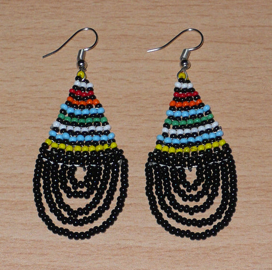 Boucles d'oreilles ethniques de tradition sud-africaine en forme de gouttes composées d'un tissage de perles de rocaille noires et multicolores. Elles mesurent 7 cm de long et 2,5 cm de large et se portent sur des oreilles percées. Timeless Fineries