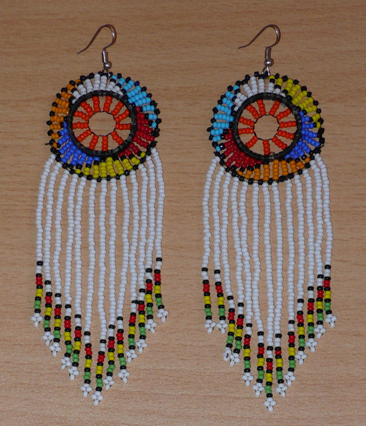 Longues boucles d'oreilles sud-africaines pendantes à franges et motifs traditionnels zoulous se composant de perles de rocaille blanches, orange et multicolores enfilées sur des fils de nylon.  Ces boucles d'oreilles afro bohème mesurent 14,5 cm de long et 4,5 cm de large ; elles se portent avec des crochets en acier inoxydable sur des oreilles percées.