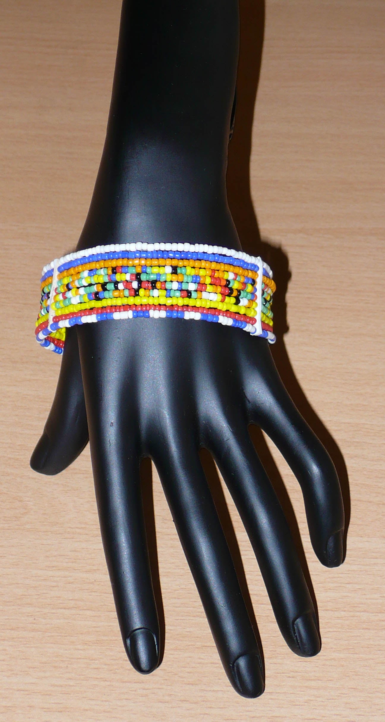 Bracelet africain Massai composé de dix rangées de perles multicolores enfilées sur des fils de fer fixés sur des charnières en plastique. Le bracelet se ferme avec deux crochets.