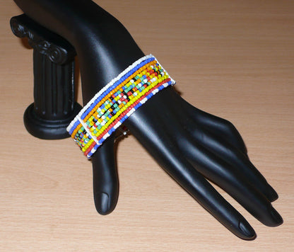 Bracelet africain Massai composé de dix rangées de perles multicolores enfilées sur des fils de fer fixés sur des charnières en plastique. Le bracelet se ferme avec deux crochets.