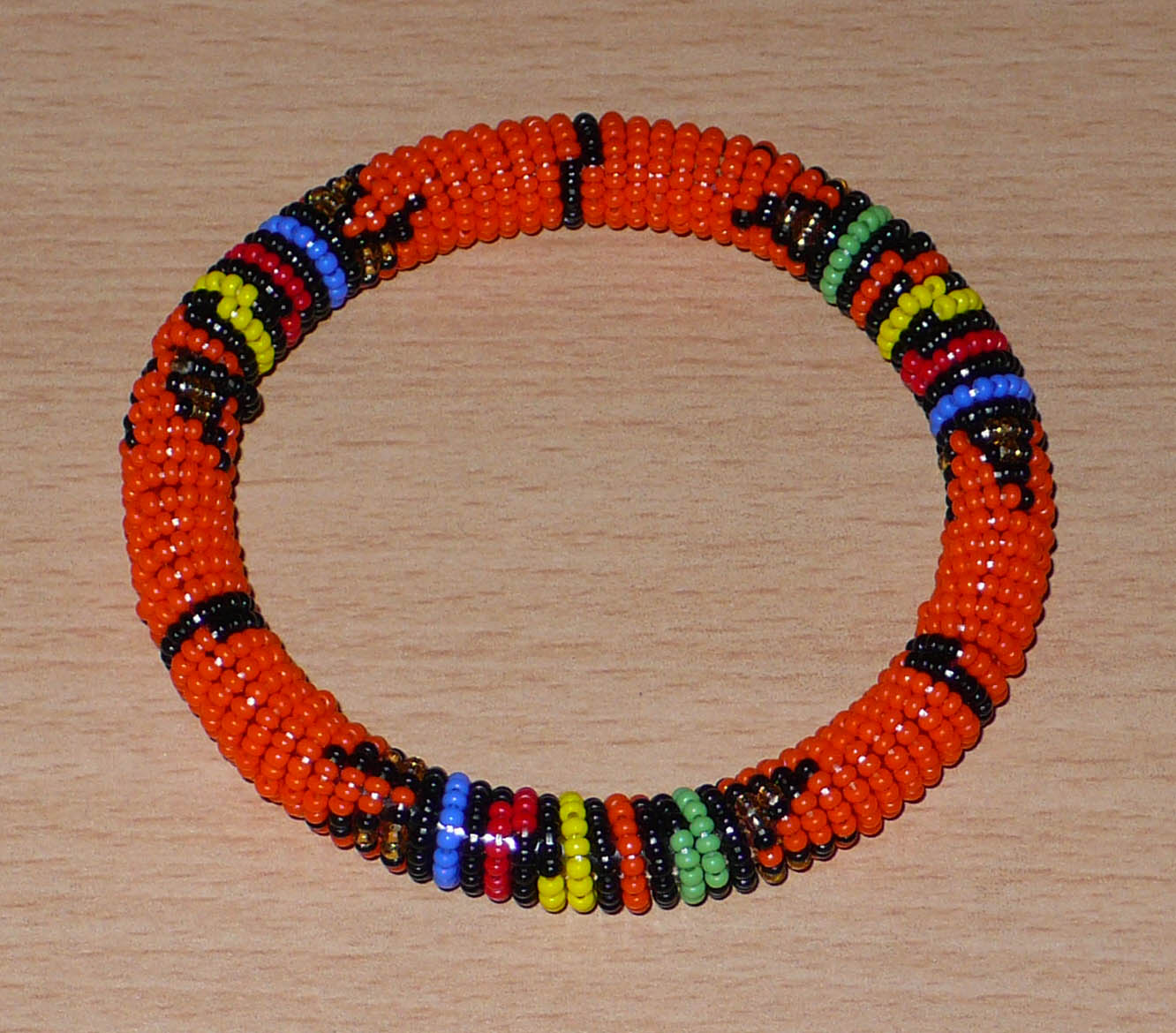 Bracelet africain traditionnel à motifs ethniques zoulous en perles de rocaille orange et multicolores enfilées sur du fil de nylon enroulé autour d'un tube en plastique.
La circonférence interne de ce bracelet est de 21 cm, son diamètre interne de 6.5 cm, et son épaisseur de 1 cm.
Bracelet unisexe pouvant être porté par une femme ou par un homme.