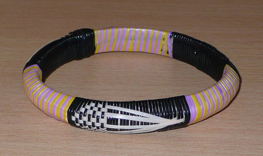 Bracelet africain à motifs ethniques ; conçu dans une approche écologique, il est tissé avec des bandes de plastique recyclé noir, blanc, jaune et parme.  Ce bracelet taille grand, avec une circonférence de 23 cm, un diamètre de 7,5 cm et une épaisseur de 1,3 cm.  Il peut être porté par une femme ou par un homme.