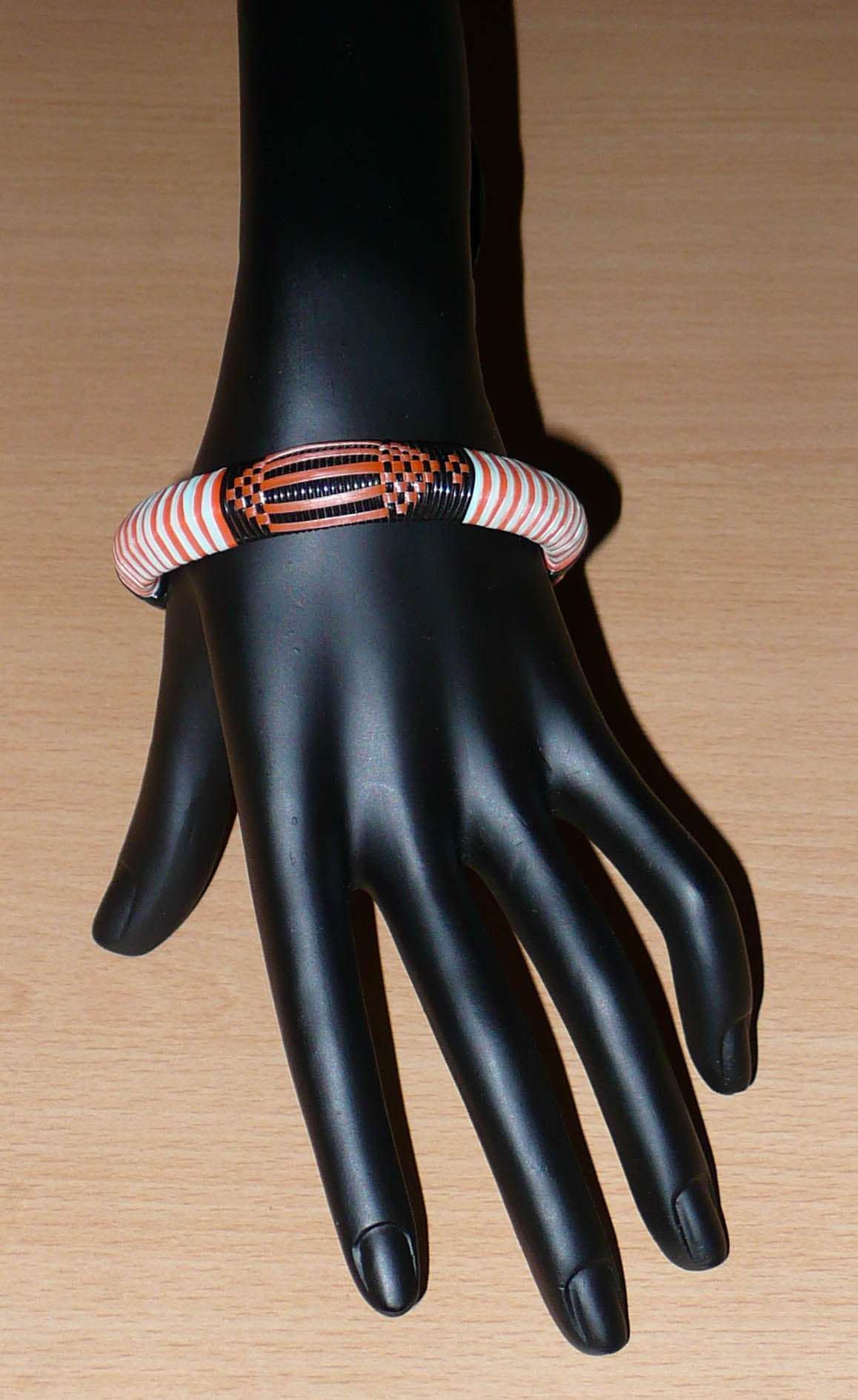 Bracelet africain tribal à motifs ethniques tressés avec du plastique recyclé orange, noir et bleu ciel.

Ce bracelet a une circonférence de 20 cm, un diamètre de 6 cm et une épaisseur de 1.2 cm ; il peut être porté par une femme ou par un homme.