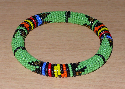 Bracelet africain tubulaire à motifs tribaux zoulous fait de perles de rocaille vertes et multicolores glissées sur du fils de nylon enroulé autour d'un tube en plastique.
Ce bracelet a une circonférence de 21 cm, un diamètre de 6.5 cm et une épaisseur de 1 cm.
Il peut être porté par une femme ou par un homme.