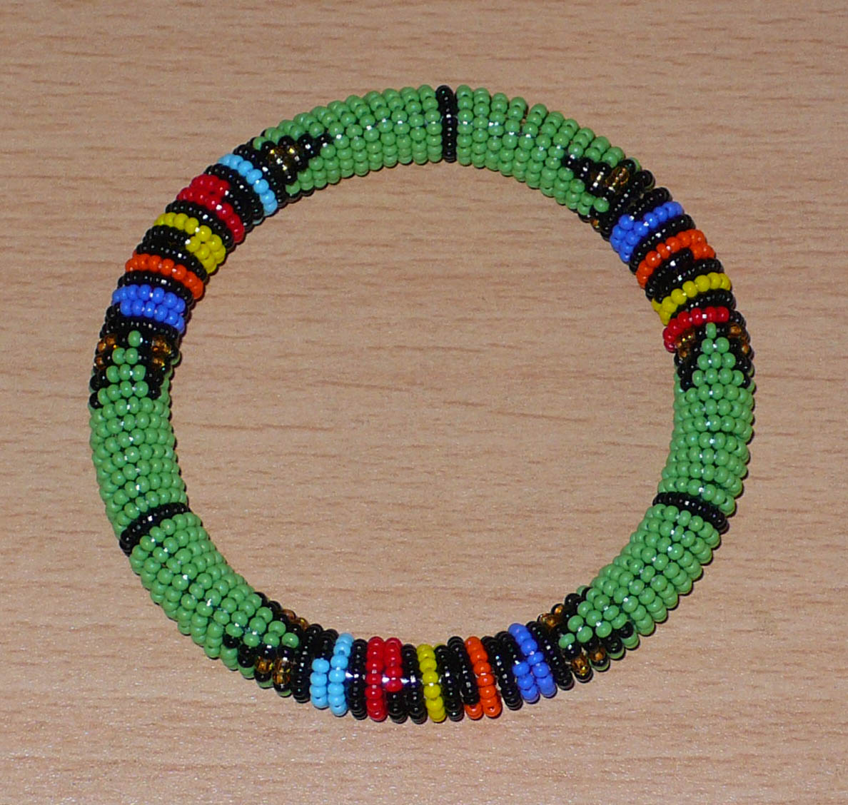 Bracelet africain tubulaire à motifs tribaux zoulous fait de perles de rocaille vertes et multicolores glissées sur du fils de nylon enroulé autour d'un tube en plastique.
Ce bracelet a une circonférence de 21 cm, un diamètre de 6.5 cm et une épaisseur de 1 cm.
Il peut être porté par une femme ou par un homme.