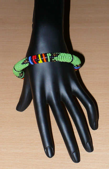 Bracelet africain tubulaire à motifs tribaux zoulous fait de perles de rocaille vertes et multicolores glissées sur du fils de nylon enroulé autour d'un tube en plastique.
Ce bracelet a une circonférence de 21 cm, un diamètre de 6.5 cm et une épaisseur de 1 cm.
Il peut être porté par une femme ou par un homme.