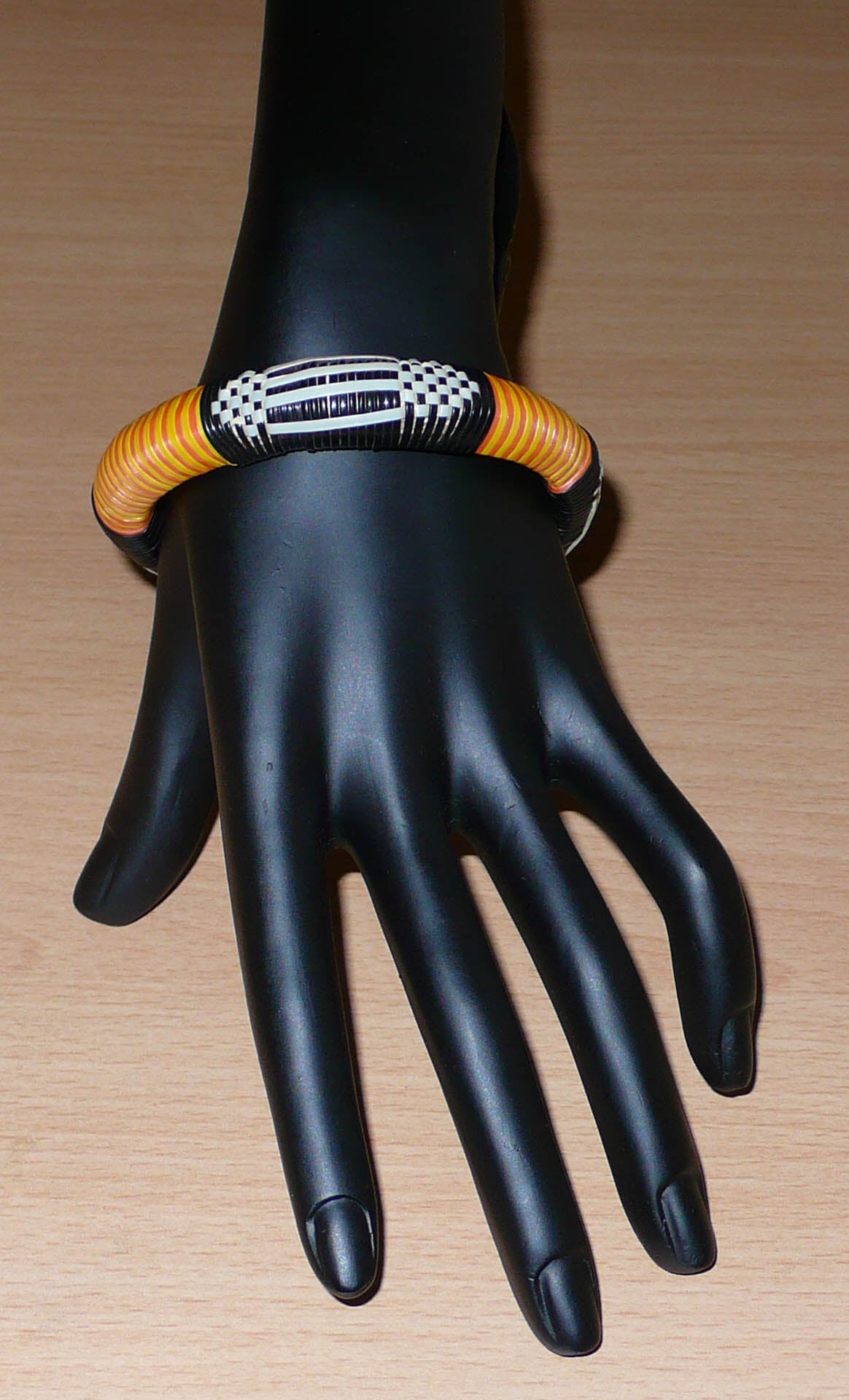 Fabriqué au Mali dans une démarche écolo friendly, ce bracelet africain se compose de motifs ethniques tissés à partir de fines bandes de plastique recyclé noir, blanc, jaune et orange. La circonférence interne du bracelet est de 20 cm, son diamètre de 6,5 cm pour une épaisseur de 1,3 cm.
