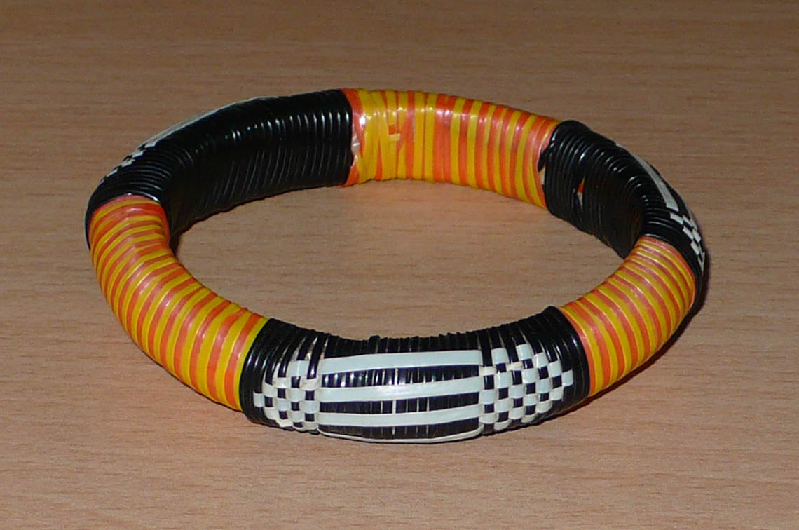Fabriqué au Mali dans une démarche écolo friendly, ce bracelet africain se compose de motifs ethniques tissés à partir de fines bandes de plastique recyclé noir, blanc, jaune et orange. La circonférence interne du bracelet est de 20 cm, son diamètre de 6,5 cm pour une épaisseur de 1,3 cm.