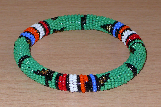 Bracelet africain tubulaire à motifs ethniques zoulous fait de perles de rocaille vertes et multicolores glissées sur du fils de nylon enroulé autour d'un tube en plastique.  Ce bracelet peut être porté par une femme ou par un homme ; il a une circonférence de 21 cm, un diamètre de 6,5 cm et une épaisseur de 1 cm.