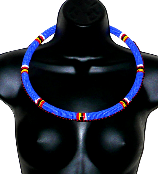 Bijou africain traditionnel. Collier africain Massai tubulaire composé de perles de rocaille principalement bleues et de motifs fait de perles rouges, jaunes, blanches et noires enroulées sur un tube en plastique. Ce collier mesure 29,5 cm de long, sa longueur autour du cou est de 68 cm et son épaisseur de 1,5 cm ; il s'attache avec un crochet. Timeless Fineries