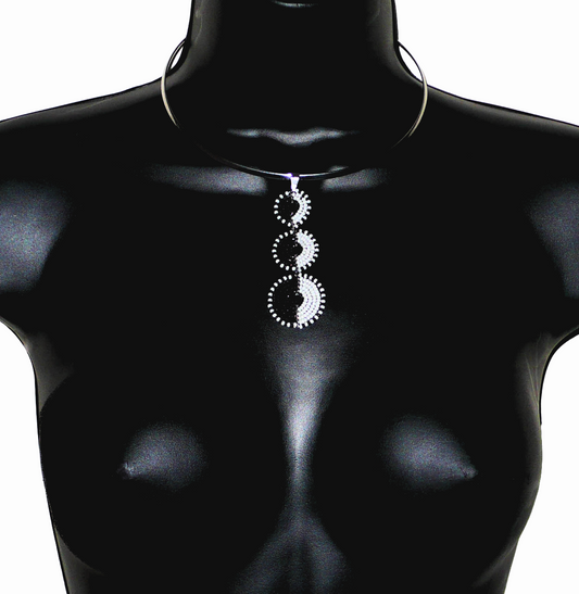 Bijou ethnique contemporain. Collier africain composé d'un ras-de-cou en laiton argenté rehaussé d'un long et fin pendentif fait de trois cercles superposés en perles de rocaille noires et blanches. Ce collier mesure 22 cm de long, le tour de cou en laiton a une circonférence de 42,5 cm et un diamètre de 13,5 cm ; le pendentif bicolore mesure 8 cm de long et 3 cm de large. Timeless Fineries