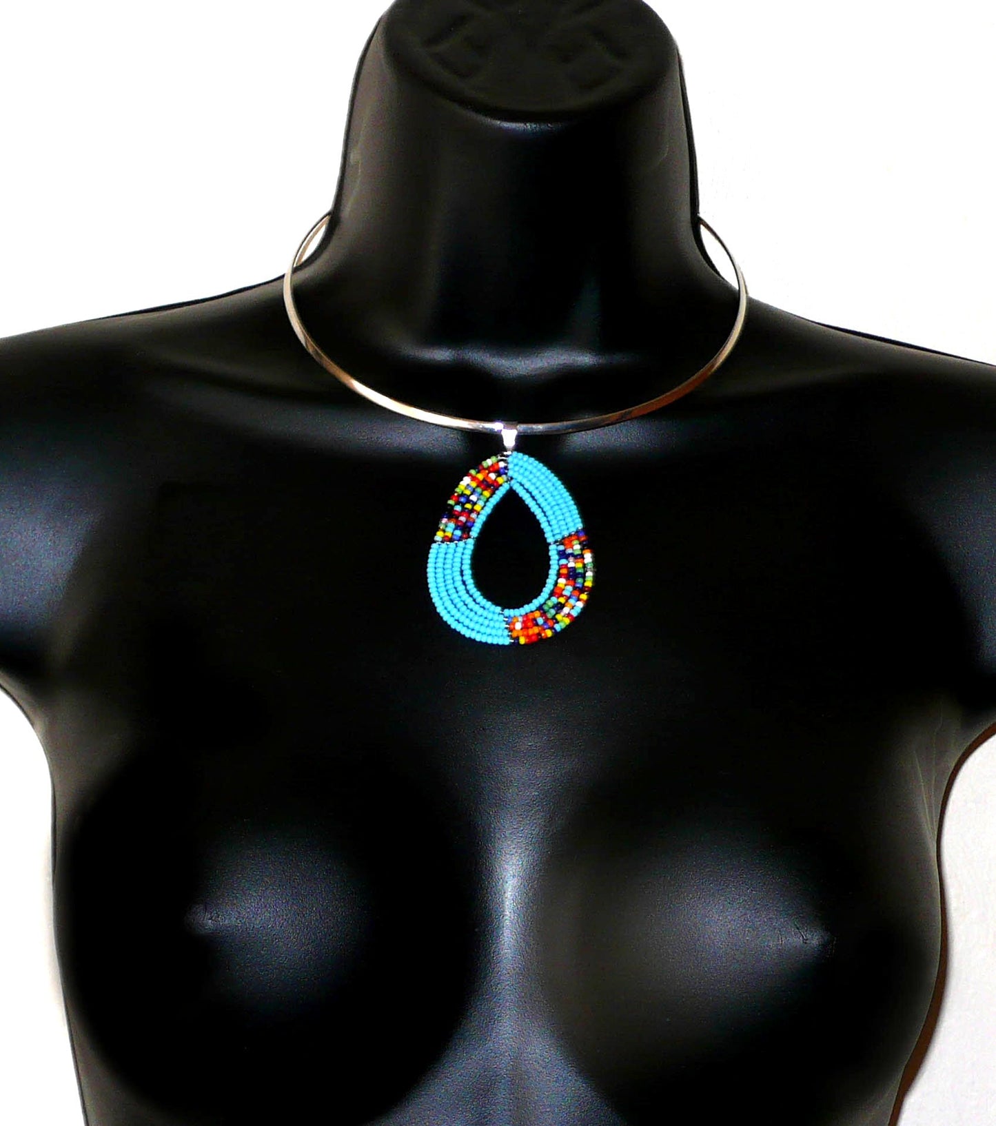 Bijou bleu. Collier Massai bohème chic se composant d'un tour de cou en laiton argenté agrémenté d'un pendentif fait de perles de rocaille bleu ciel et multicolores enfilées sur cinq rangs de fils de fer montés en forme de goutte. Ce collier mesure 19,5 cm de long (de la nuque jusqu'à la base du pendentif), la circonférence du ras-de-cou est de 42,5 cm pour un diamètre de 13,5 cm ; le pendentif mesure 6 cm de long et 4,5 cm de large.