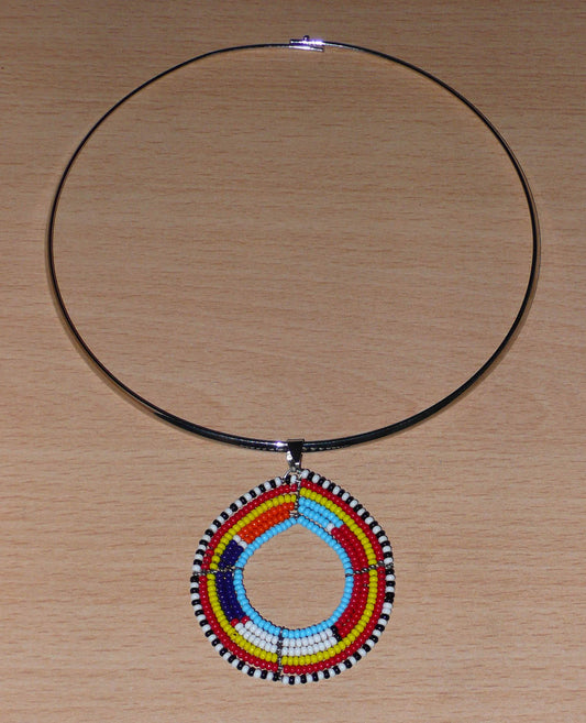 Collier africain au style ethnique chic rétro des années 70 composé d'un ras-de-cou en laiton argenté rehaussé d'un médaillon traditionnel Massai fait de perles de rocaille multicolores glissées sur six rangées de fils de fer montés en cercles.  Ce collier mesure 19.5 cm de long (de la nuque jusqu'au pendentif), le ras-de-cou en laiton a une circonférence de 42.5 cm et un diamètre de 13.5 cm ; le médaillon perlé mesure 5 cm de long et de large.