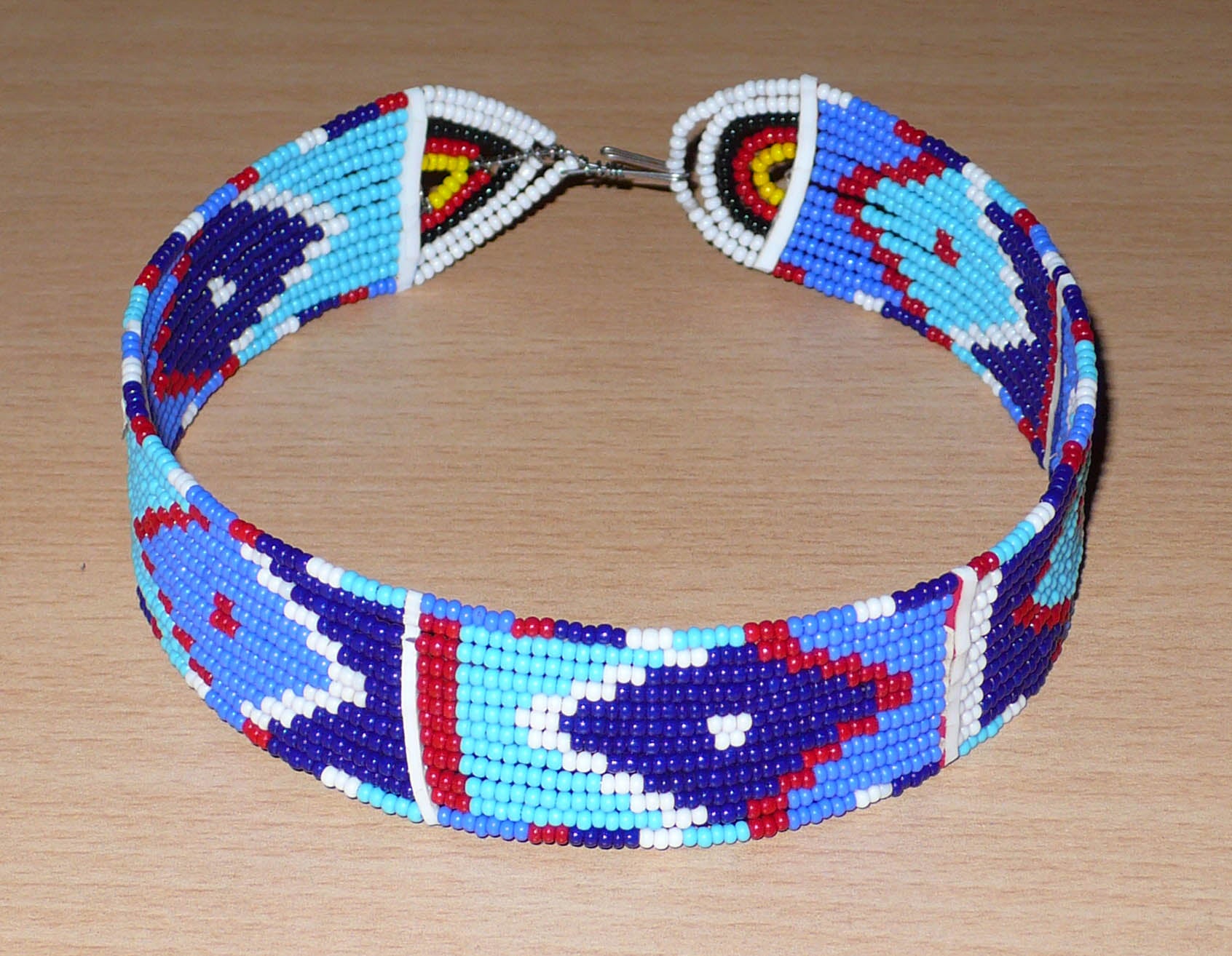 Collier ras de cou africain à motifs ethniques Massai composé de douze rangées de perles de rocaille principalement bleues rouges et blanches ; il se ferme avec un crochet.