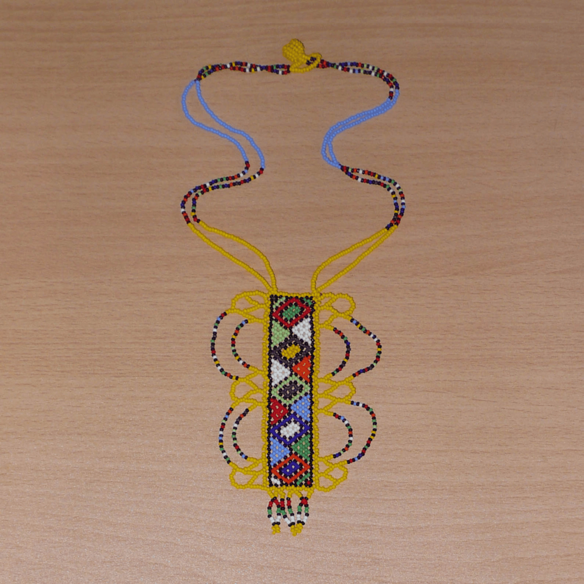 Collier africain jaune orné d'un long pendentif décoré de motifs ethniques zoulous multicolores composé de perles de rocaille. 