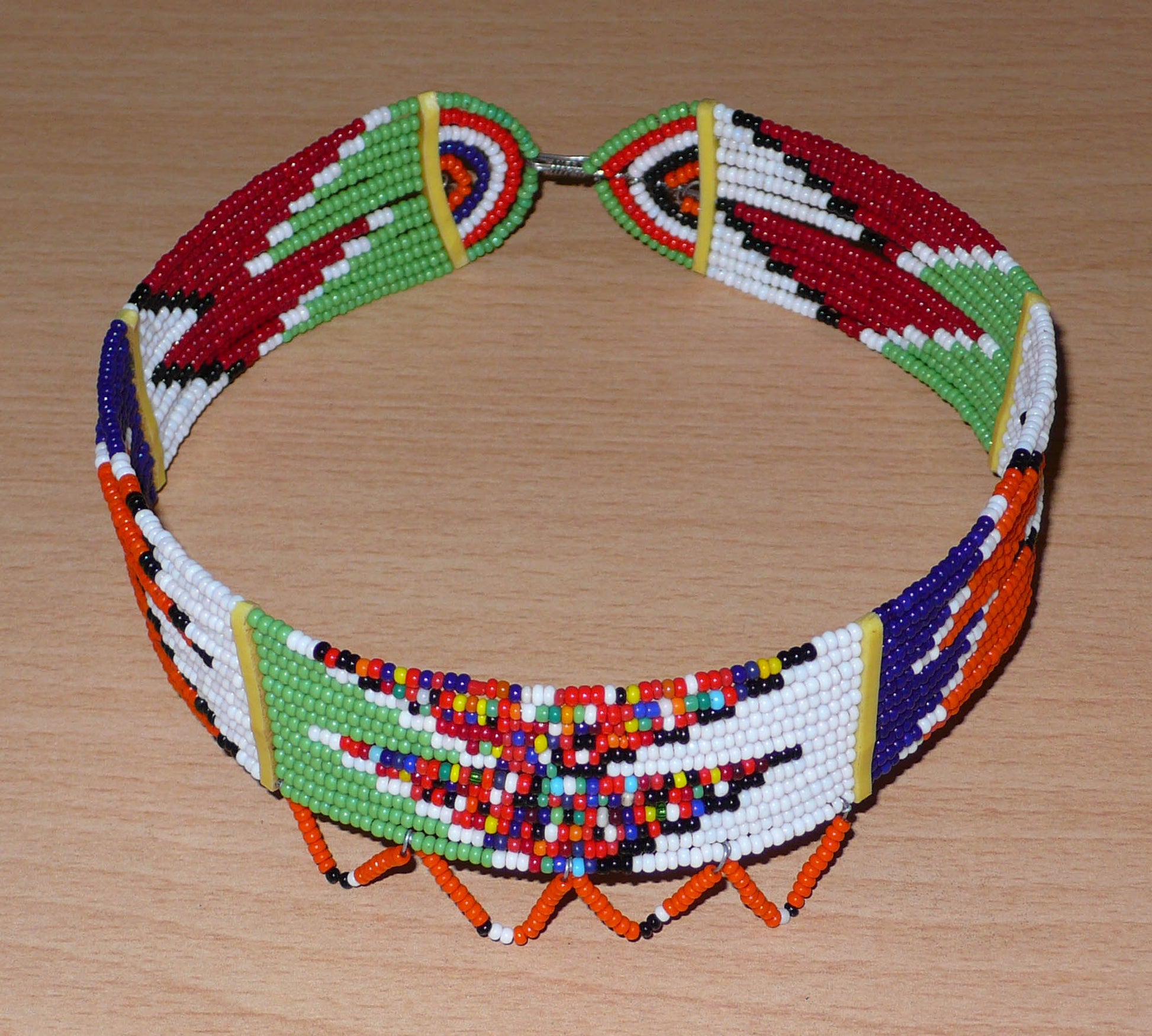 Collier ras de cou africain de tradition Massai fait de douze rangées de perles de rocaille multicolores enfilées sur des fils de fer insérés dans des charnières en plastique. Le collier est décoré à sa base d'une frise perlée et se ferme avec un crochet.

Ce collier ethnique mesure 40 cm de long et 12.5 cm de diamètre ; il a une largeur de 3 cm et de 4 cm en comptant la frise perlée.