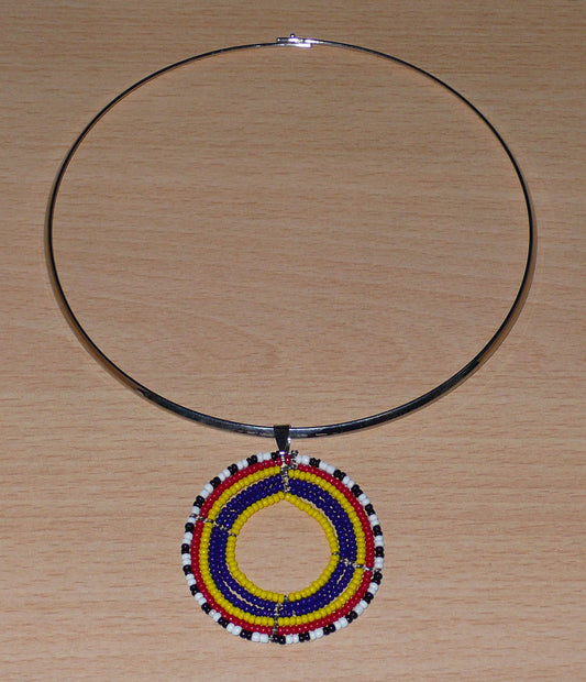 Collier africain composé d'un ras de cou en laiton argenté orné d'un médaillon Massai fait de perles de rocaille bleu foncé, rouges, jaunes, blanches et noires glissées sur une structure circulaire de fils de fer. Il mesure 19 cm de long, en partant de la nuque jusqu'au pendentif, le ras de cou en laiton a une circonférence de 42,5 cm et un diamètre de 13,5 cm ; le médaillon mesure 5 cm de long et de large.