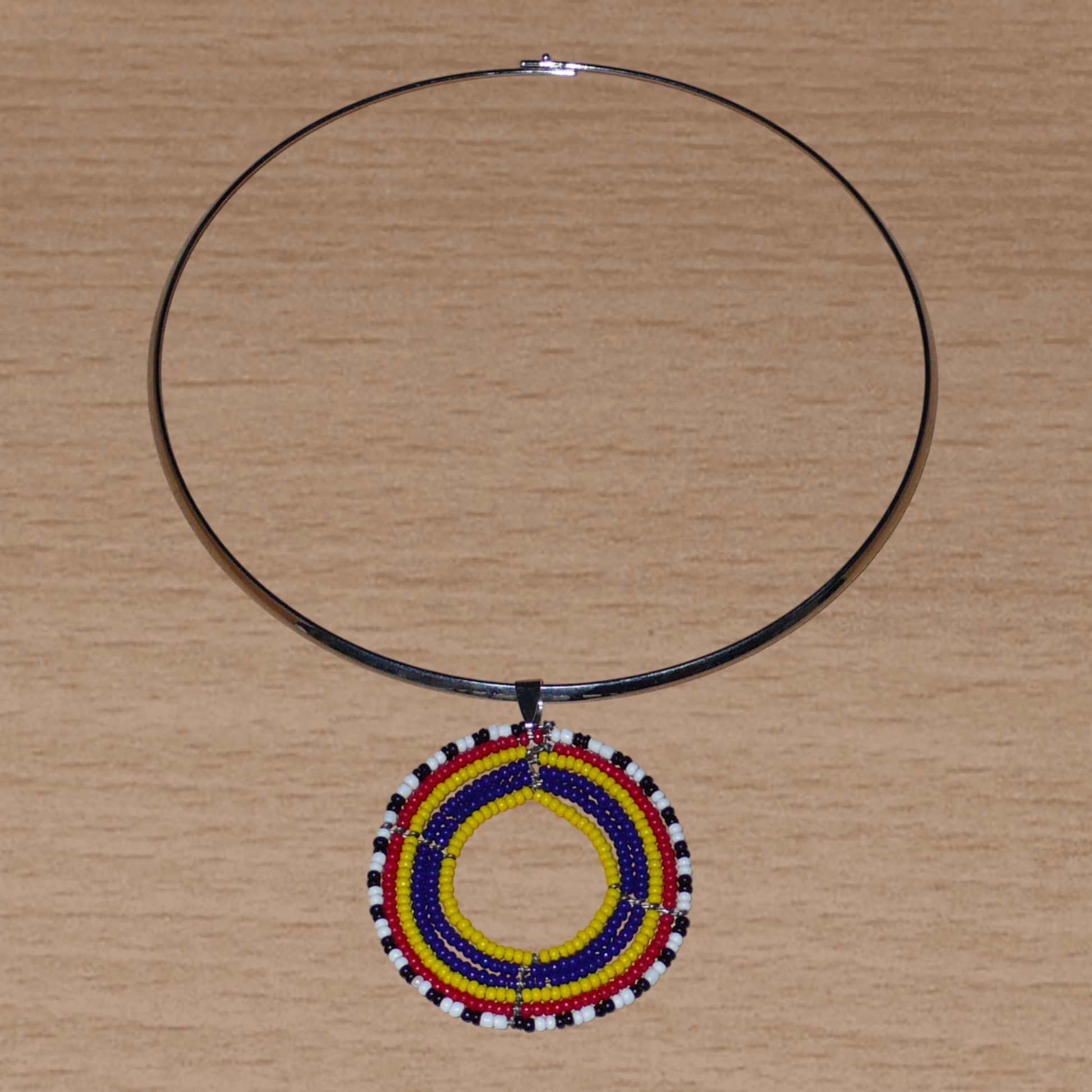 Collier ethnique aux accents afro bohème composé d'un ras de cou en laiton orné d'un médaillon Massai fait de perles de rocaille bleu foncé, jaunes, rouges, blanches et noires.