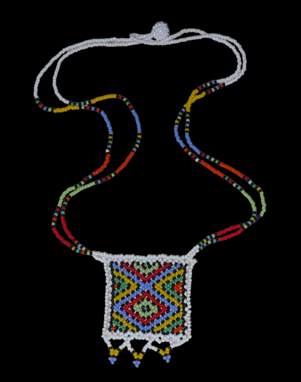 Collier africain traditionnel orné d'un pendentif décoré de motifs ethniques sud-africains ; il se compose d'un tissage de perles de rocaille blanches et multicolores et s'attache avec un fermoir à boule. Ce collier mesure 28,5 cm de long (de la nuque au pendentif), la longueur de chaîne autour du cou est de 50 cm ; le pendentif carré orné d'une frise perlée mesure 5,5 cm sur 4,5 cm.
