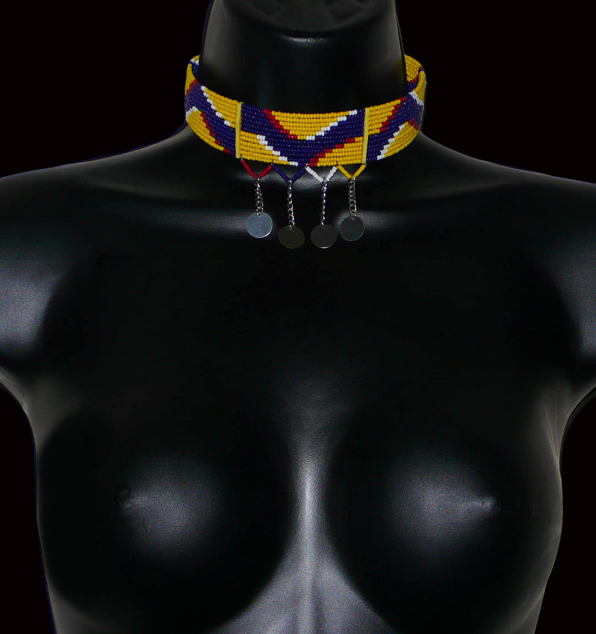 Collier ras de cou ethnique de tradition Massai fait de douze rangées de perles de rocaille jaunes, bleu foncé, rouges et blanches enfilées sur des fils de fer glissés dans des charnières en plastique jaune. Le collier est décoré chaînettes prolongées par des pastilles métalliques ; il se ferme avec un crochet.