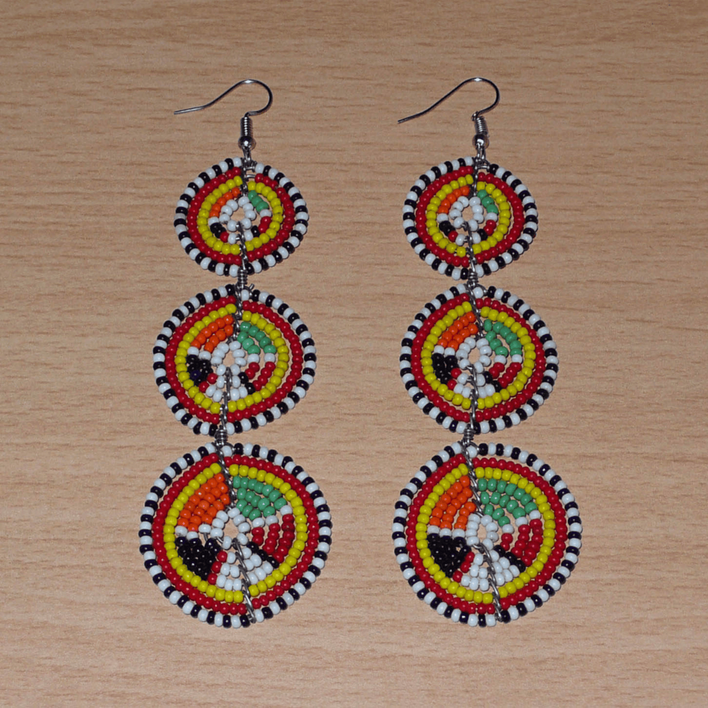 Longues boucles d'oreilles africaines composées de trois cercles superposés en perles de rocaille multicolores. Elles mesurent 11 cm de long et 3 cm de large et se portent avec des crochets en acier inoxydable sur des oreilles percées.