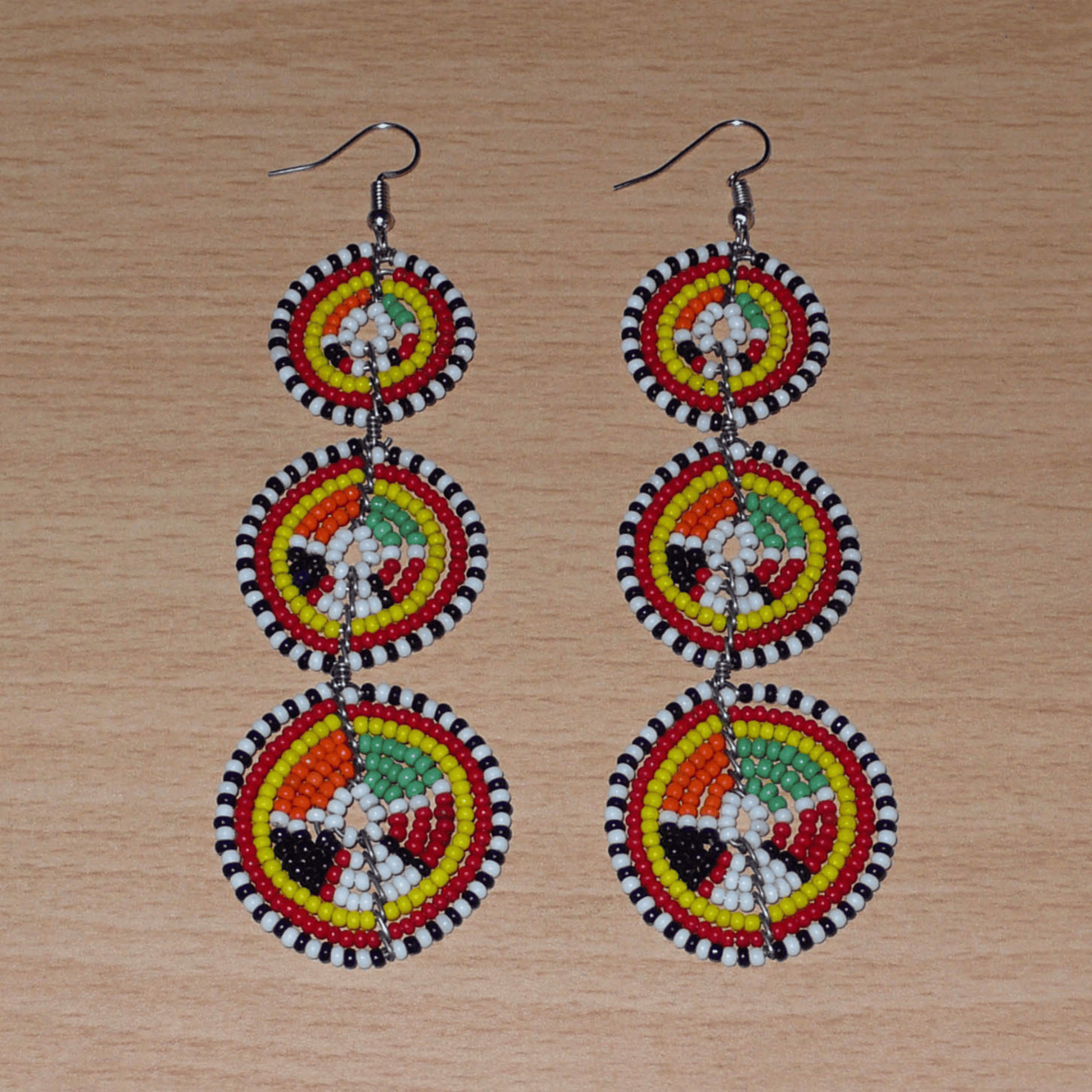 Longues boucles d'oreilles africaines composées de trois cercles superposés en perles de rocaille multicolores. Elles mesurent 11 cm de long et 3 cm de large et se portent avec des crochets en acier inoxydable sur des oreilles percées.