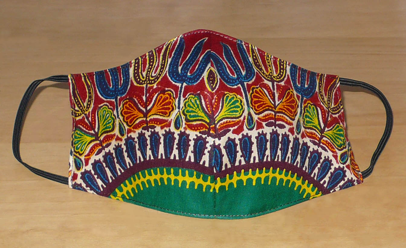 Masque facial coupé et cousu dans un tissu africain imprimé de motifs ethniques multicolores, il se porte avec des élastiques. À utiliser de manière éco-responsable, ce masque est lavable et réutilisable.  Ce masque textile mesure 21 cm de long, et 40 cm en comptant les élastiques ; a une hauteur de 12 cm (du haut du nez jusqu'au menton) et une largeur sur les côtés de 7 cm.  Il peut être porté par une femme ou par un homme.