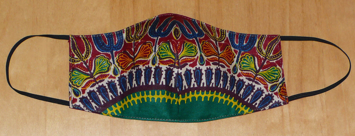 Masque facial coupé et cousu dans un tissu africain imprimé de motifs ethniques multicolores, il se porte avec des élastiques. À utiliser de manière éco-responsable, ce masque est lavable et réutilisable.  Ce masque textile mesure 21 cm de long, et 40 cm en comptant les élastiques ; a une hauteur de 12 cm (du haut du nez jusqu'au menton) et une largeur sur les côtés de 7 cm.  Il peut être porté par une femme ou par un homme.