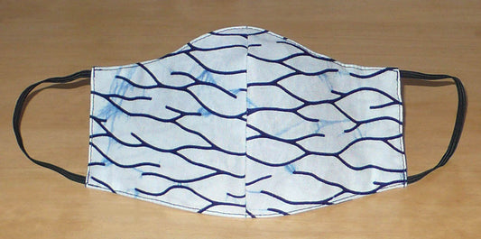 Masque textile en coton ajusté cousu dans une cotonnade blanche imprimée de motifs bleus ; il se porte avec des élastiques. En vue d'une utilisation éco-responsable, ce masque est lavable et réutilisable.