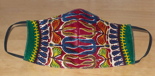 Masque facial textile ajusté en tissu africain imprimé de motifs ethniques multicolores ; il se porte avec des élastiques. En vue d'une utilisation eco-friendly, ce masque est lavable et réutilisable.  Ce masque à l'allure exotique mesure 21 cm de long, et 40 cm en comptant les élastiques ; il a une hauteur de 12 cm (du haut du nez jusqu'au menton) et une largeur sur les côtés de 7 cm.  Il peut être porté par une femme ou par un homme.  Pour des raisons évidentes d'hygiène, les retours et les échanges de ma