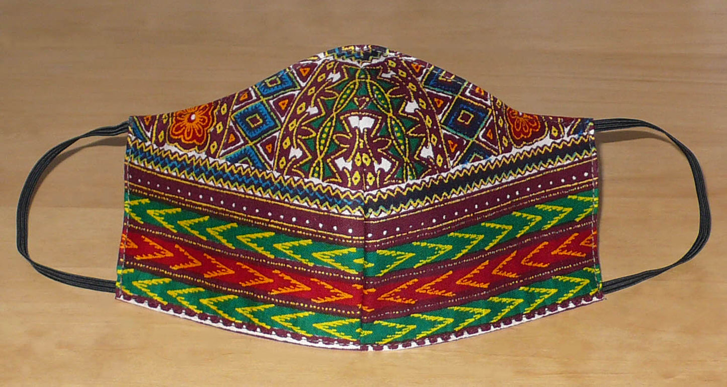 Masque textile à la coupe ajustée en tissu africain en coton imprimé de motifs ethniques multicolores ; il se porte avec des élastiques. En vue d'une utilisation eco-friendly, ce masque est lavable et réutilisable.  D'allure afro chic, ce masque mesure 21 cm de long, et 40 cm en comptant les élastiques ; il a une hauteur de 12 cm (du haut du nez jusqu'au menton) et une largeur sur les côtés de 7 cm.  Unisexe, il peut être porté par une femme ou par un homme.