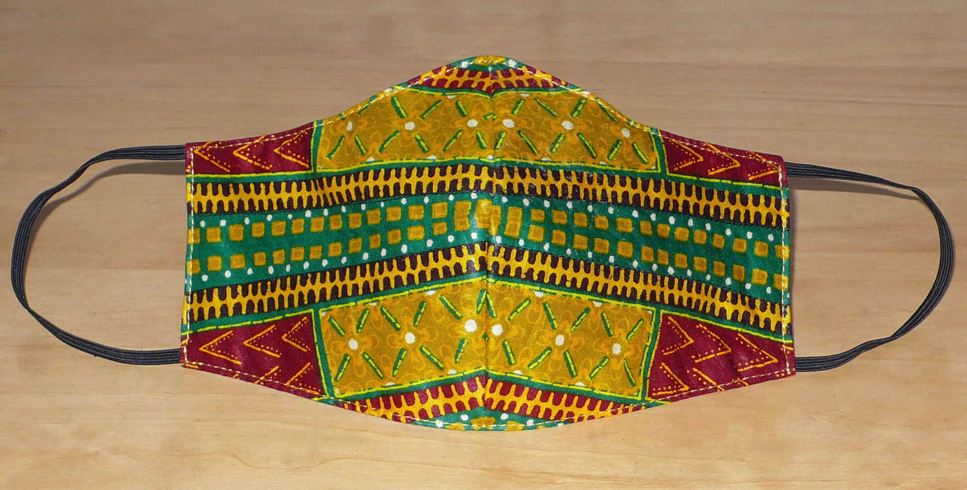 Masque de protection coupé et cousu dans un tissu en coton à motifs africains lavable et réutilisable. Il se porte avec des élastiques.